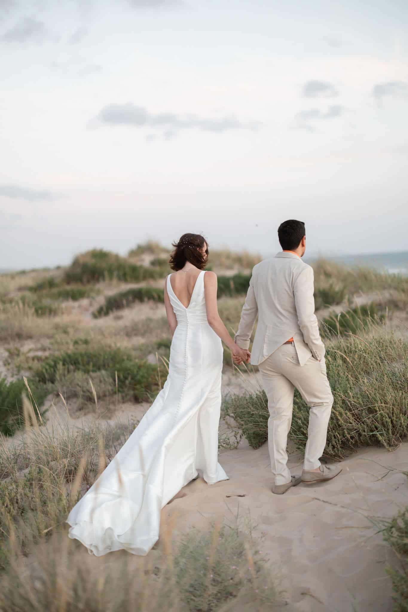 Lily and Michael walking hand in hand along a sandy path near the coast.