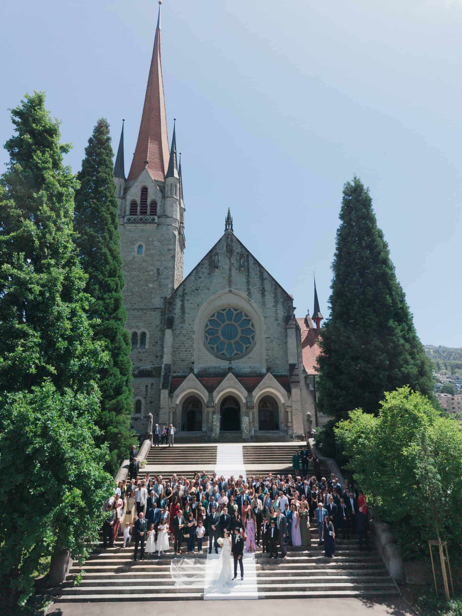 Aerial view of the church used for Francesca and Giuseppe’s wedding in Zug, with a tall red spire and guests outside.