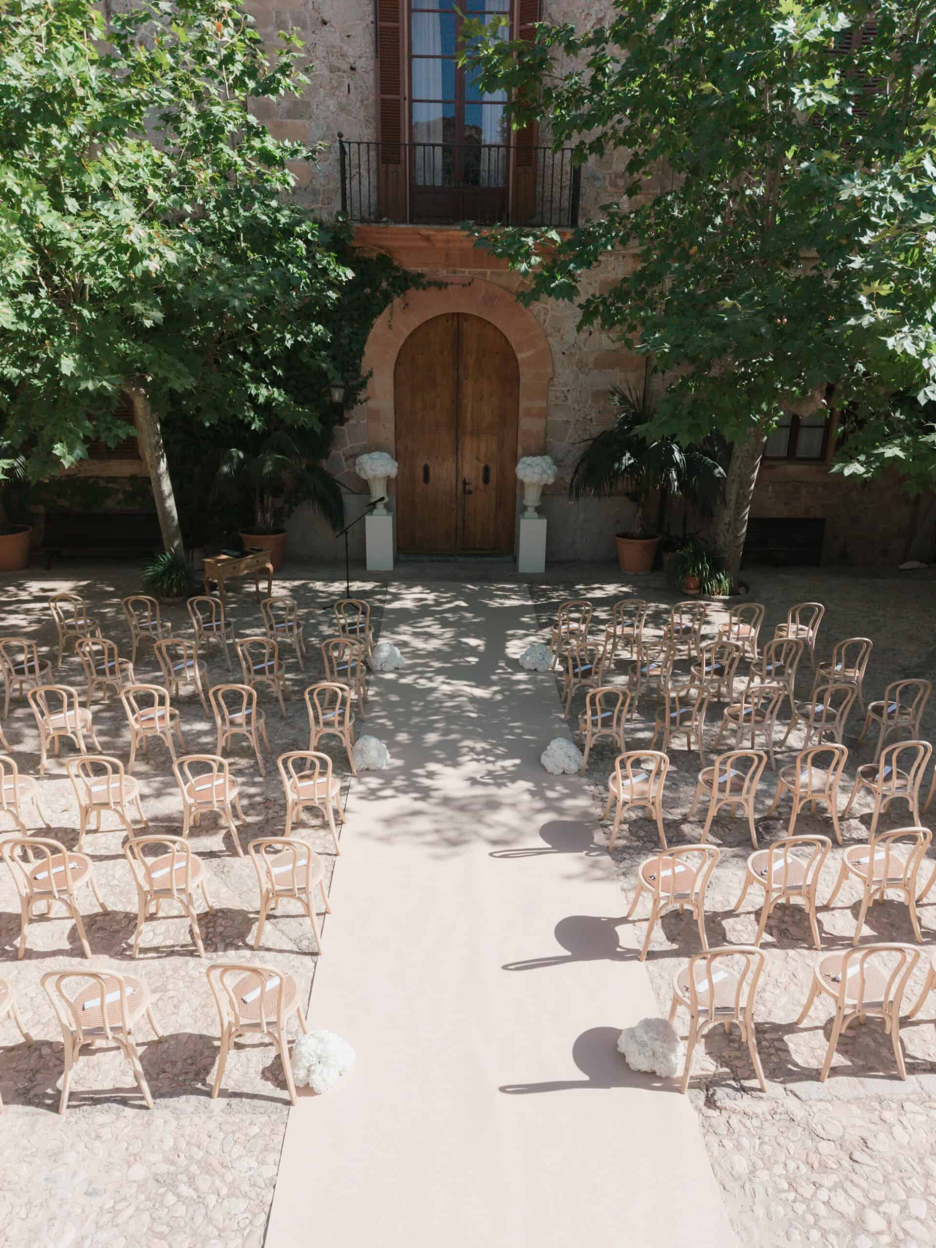 Courtyard wedding ceremony at Son Togores in Mallorca, with white aisle flowers and wooden chairs.