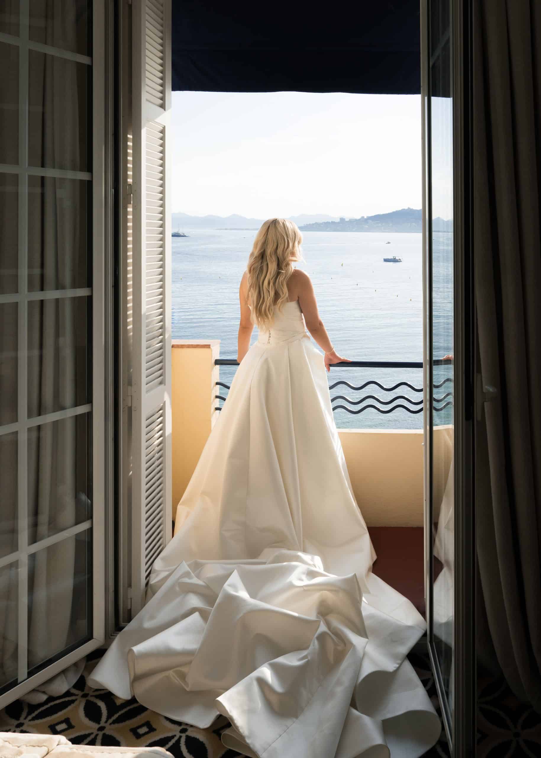 Bride with a long wedding dress train framed by open doors overlooking the Mediterranean.