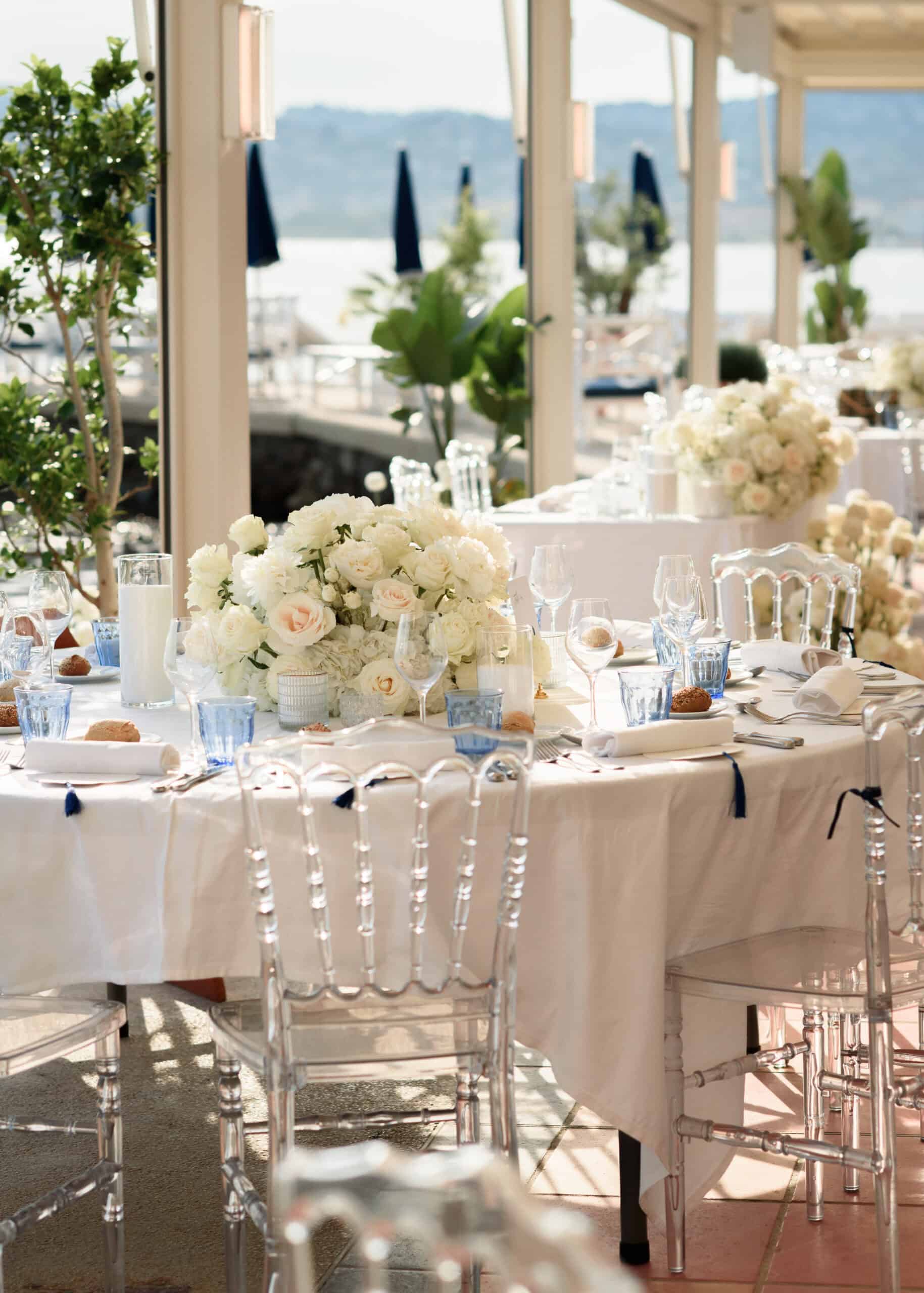 Reception tables at Hôtel Belles Rives with white flowers, blue glassware and transparent chairs.