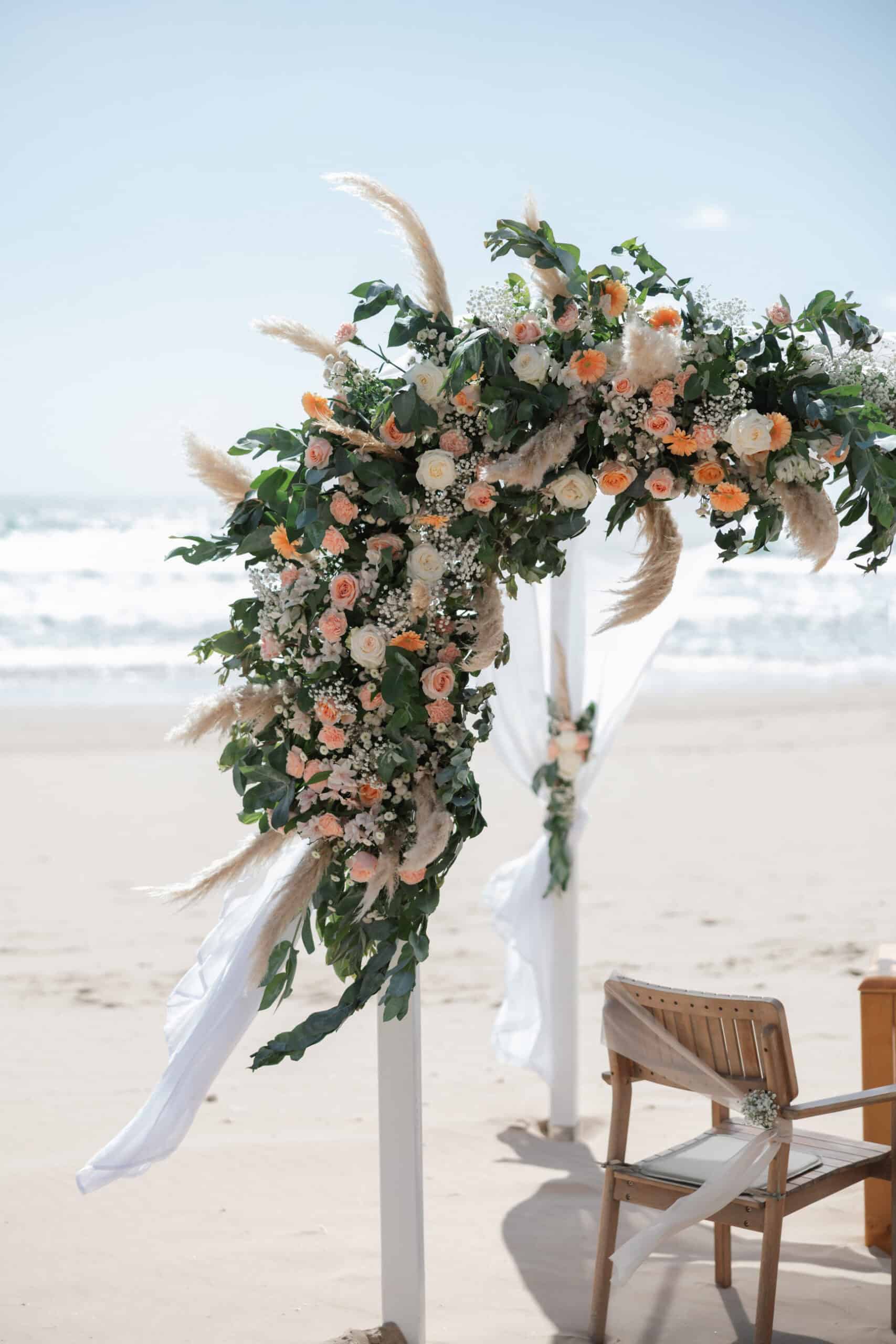 Peach and white flowers decorating a beach wedding ceremony arch in Costa da Caparica.