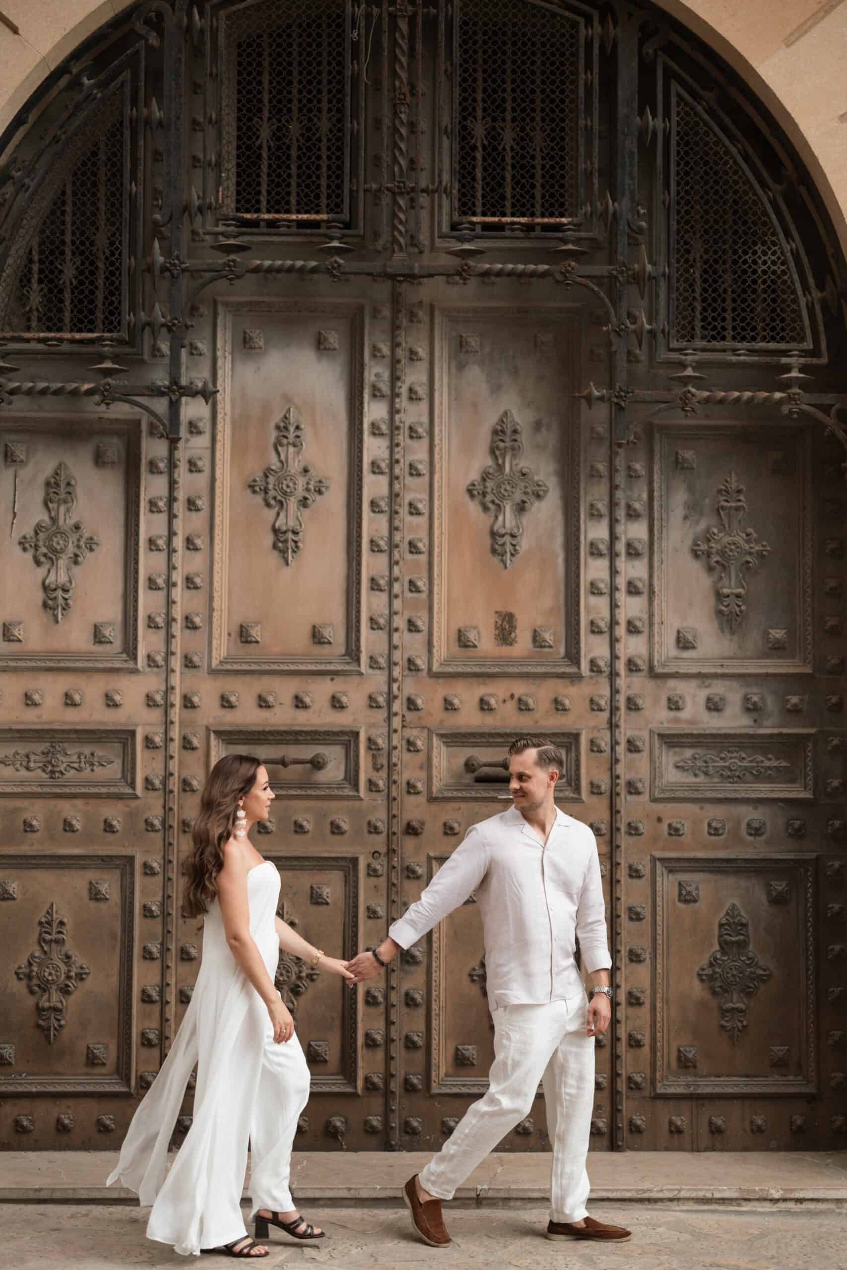 Yaiza and Stefan standing before a large carved wooden doorway in light-coloured outfits.