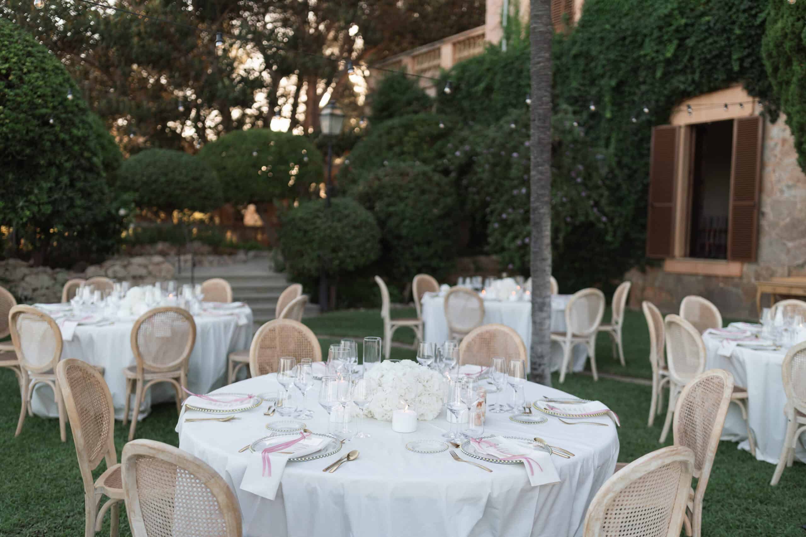 Garden wedding table at Son Togores with white flowers, pink ribbons and gold-toned cutlery.