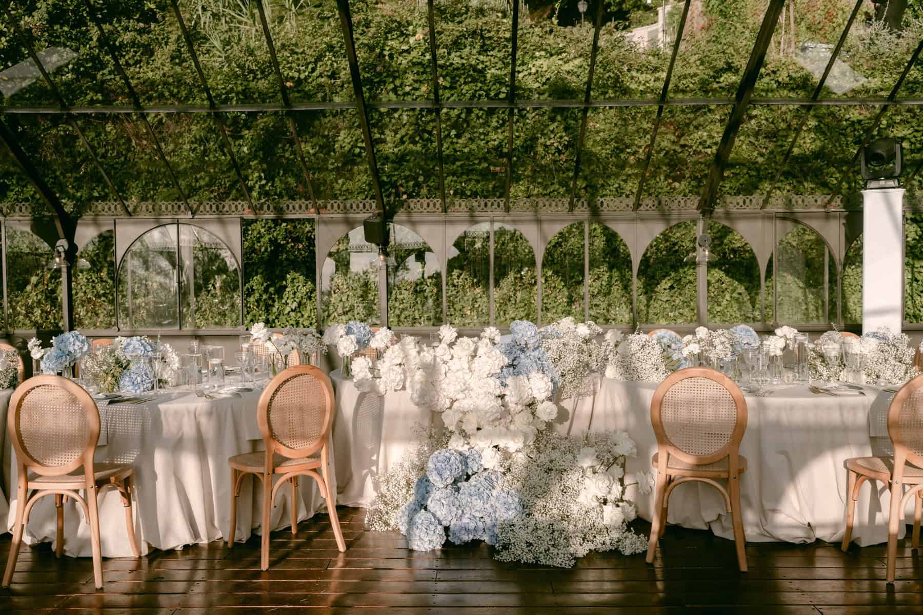 Wedding reception tables with white and pale blue flowers beneath a glass roof at Quinta da Bella Vista in Sintra.