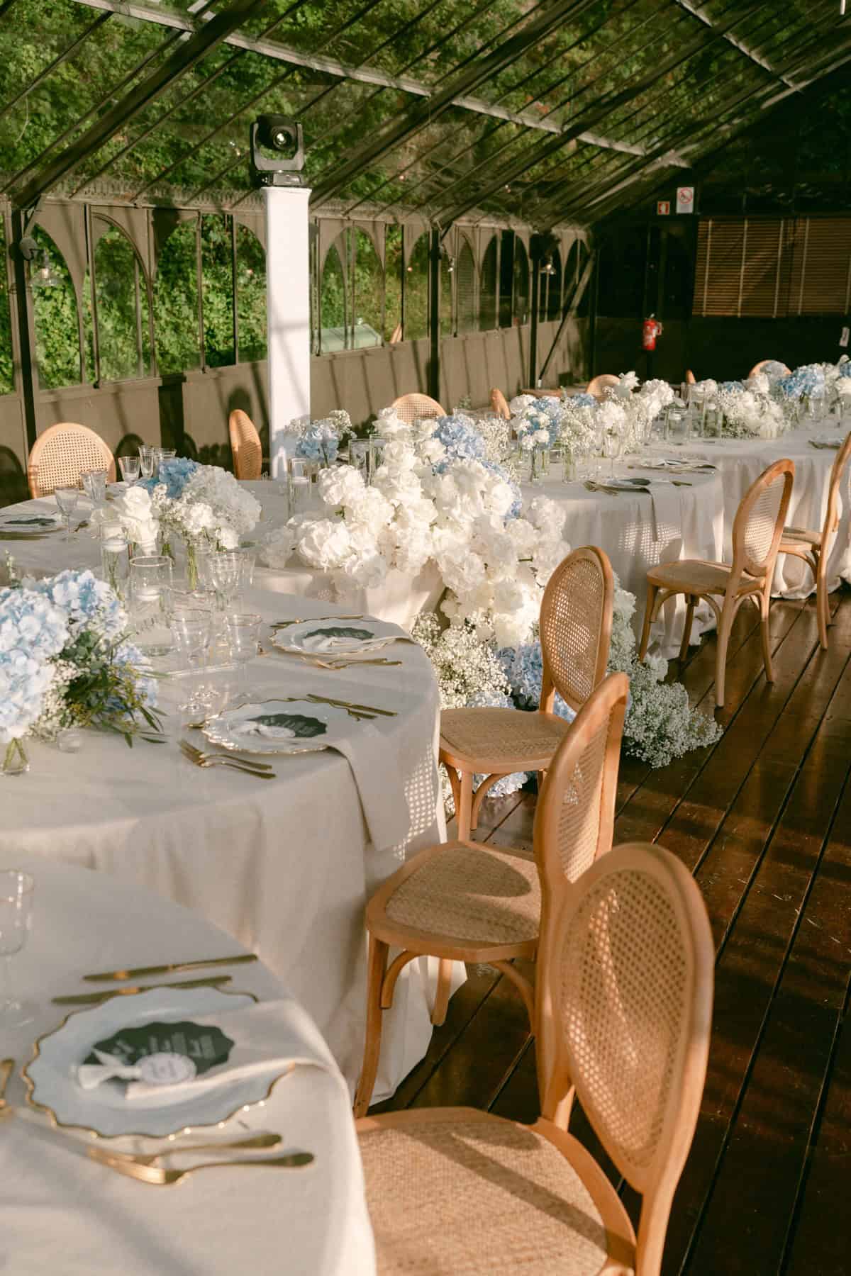 White linens, cane-backed chairs and floral arrangements at Jacqueline and Andrew’s wedding reception.